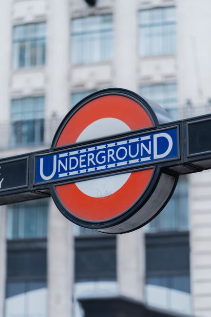 The image shows a close-up of the iconic London Underground sign with a blue rectangular bar bearing the word 'UNDERGROUND' in white lettering, positioned horizontally beneath a circular red and white