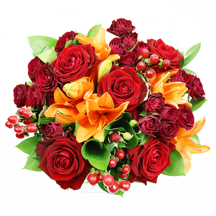 Seen in a top-down composition against a clean white backdrop, this abundant bouquet is an exercise in warm contrast and tactile luxury, composed with the eye of a seasoned florist at Flower Delivery Elm Park. Large, deep red roses dominate the scene, their velvety petals unfurling in layered spirals that convey romance and timeless sentiment. Between these bold heads, vivid orange Asiatic lilies offer trumpet-like forms and a luminous brightness; several are fully open with visible stamens and delicate throat speckling, while others hover between bud and bloom, suggesting ongoing freshness and life. Interlaced are numerous small, dark red spray roses-tight, clustered blooms that add plush texture and a richer, wine-hued depth to the palette. Shiny, round hypericum berries in a ruby-red tone appear in small clusters, providing glossy punctuation and a cheerful, tactile contrast to the soft petals. Green foliage with broad, glossy leaves-reminiscent of ruscus or salal-peeks through and frames the flowers, enhancing volume and lending a natural, garden-fresh backdrop. The lighting is soft and flattering, highlighting petal surface, subtle veining, and berry sheen without harsh shadow. The composition carries a scent of classic rose with a citrus-spicy lift from the lilies, making it suitable for anniversaries, romantic occasions, or elegant autumnal home décor. Thoughtfully designed for neighbours from Elm Park tube to Hornchurch Country Park, this bouquet balances photography-ready structure with the lived warmth of local deliveries.