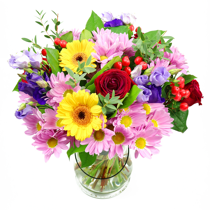 A vibrant, garden-style bouquet fills a tall clear glass vase, set simply against a white background so that every petal and leaf can be appreciated, much like pausing to admire a well-kept Elm Park front garden on a quiet side street. At the centre of the design, velvety deep red roses spiral open, their layered petals drawing the eye inward and lending the arrangement a note of heartfelt sentiment. Nearby, two sunlit yellow gerbera daisies stand proudly, each surrounded by a halo of smooth petals and anchored by a warm, dark brown-orange centre that recalls early evening light over Harrow Lodge Park. Encircling these focal blooms, soft pink daisies or chrysanthemums spread out in abundant clusters, their fine petals radiating from clear yellow centres, building up a cloud of pastel colour that gives the bouquet a sense of generosity and comfort. Slender stems of lisianthus, in shades of purple and lavender, weave through this softness, their bell-shaped, gently ruffled flowers adding cool contrast and a touch of understated elegance. Bright red hypericum berries punctuate the arrangement here and there, like small, glossy beads that invite the fingertips, introducing both colour and distinctive texture. Surrounding all of this, layers of green foliage-from broad, darker leaves to airy, lighter sprigs-wrap around the blooms, giving the design a natural framework and a feeling of freshly picked vitality. The transparent glass vase reveals straight, neatly trimmed stems fanned out in clear water, underscoring the bouquet's careful construction. Created in the spirit of local celebrations across Elm Park, this arrangement feels perfect for birthdays, new home wishes, or simply brightening a living room near The Broadway with colour and joy.